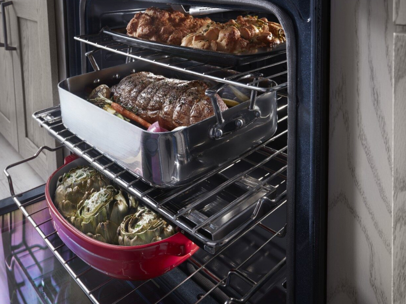 Close-up of two large meat and vegetable dishes sitting on top of extended bottom and top oven racks Close-up of two large meat and vegetable dishes sitting on top of extended bottom and top oven racks