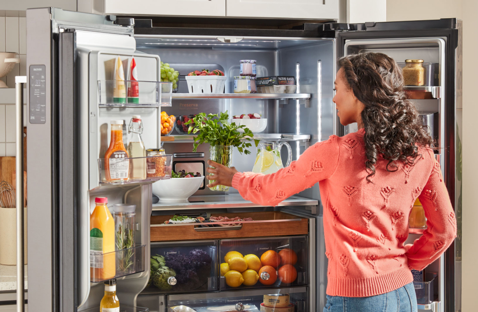 A woman placing a jar of herbs on a top refrigerator shelf. A woman placing a jar of herbs on a top refrigerator shelf.