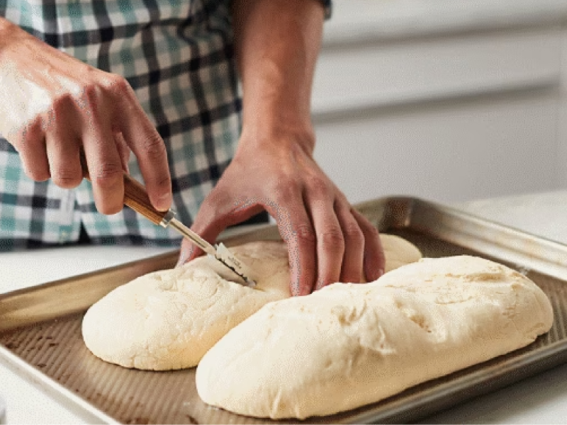 Person scoring two loaves of bread dough on a cookie sheet