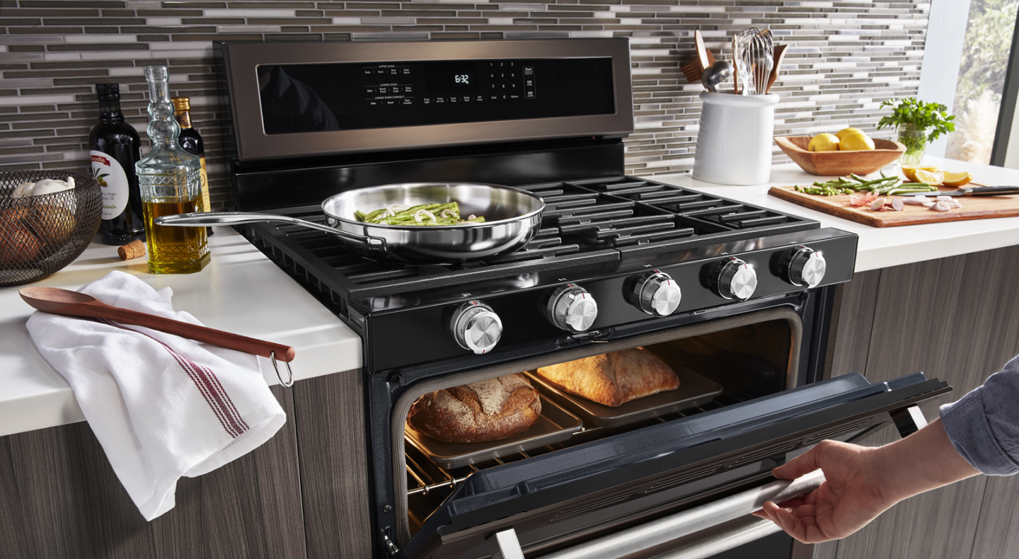Person checking on baking bread loaves in a gas oven