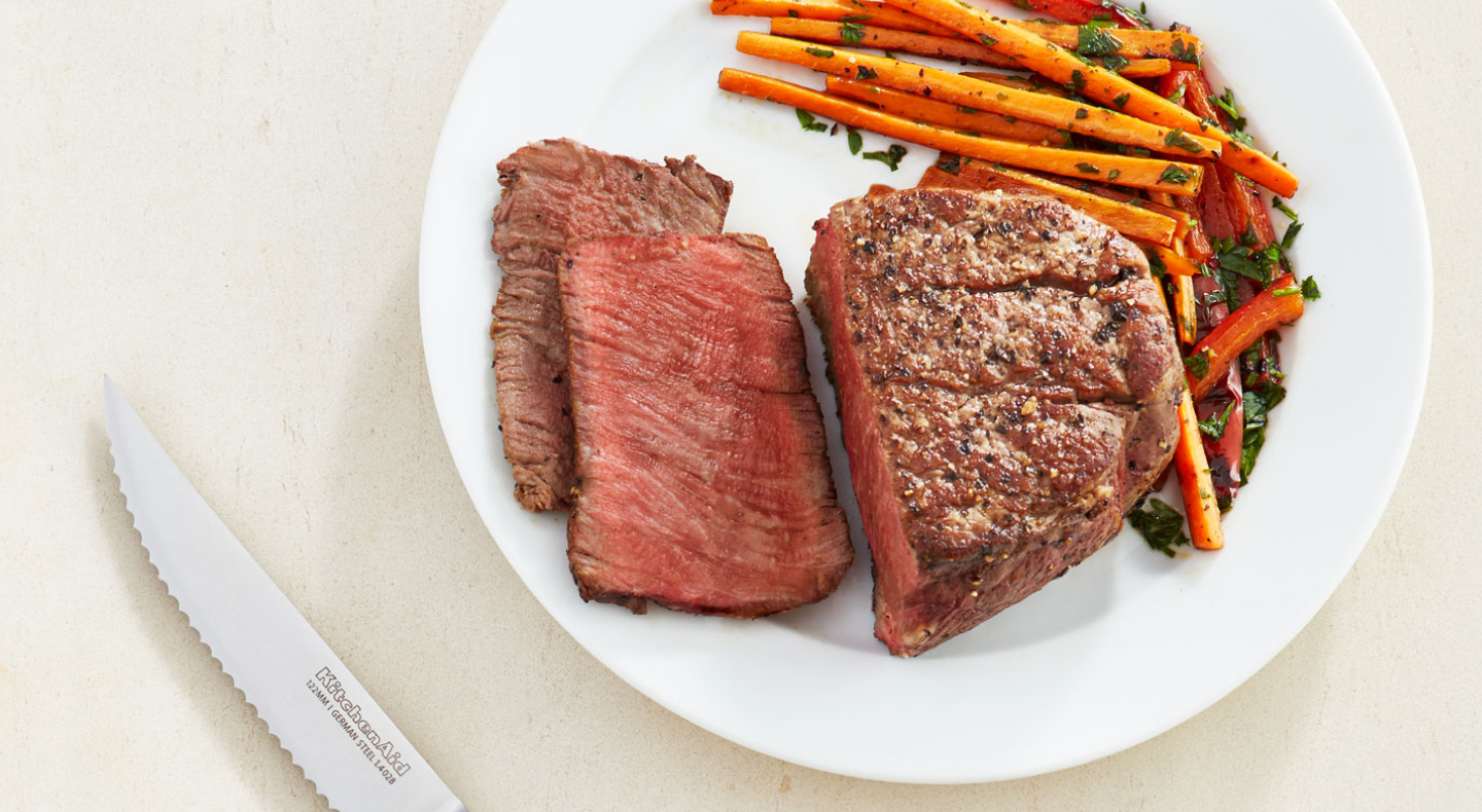 A half cut seasoned steak dish with carrots on the side A half cut seasoned steak dish with carrots on the side