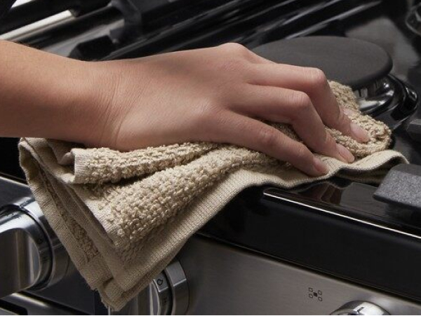 Person wiping around a stovetop burner with a tan cloth