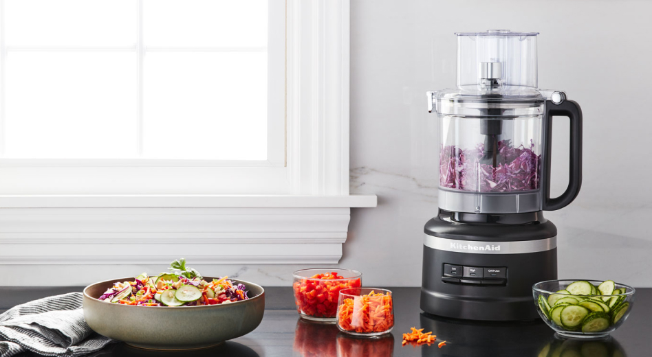 Salad topped with shredded carrots next to a black KitchenAid® food processor Salad topped with shredded carrots next to a black KitchenAid® food processor