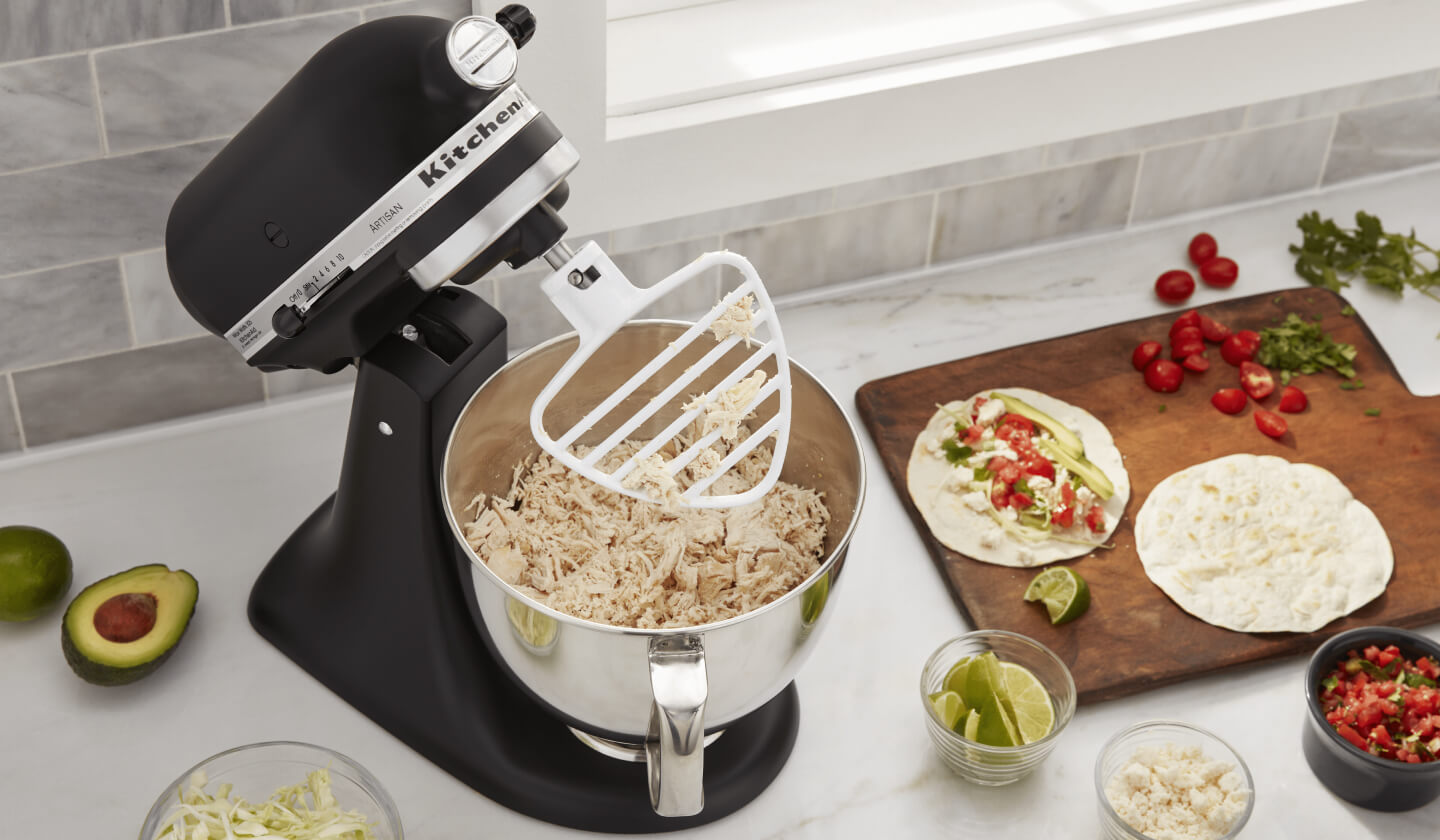 KitchenAid® stand mixer on a modern kitchen counter shredding cooked chicken. KitchenAid® stand mixer on a modern kitchen counter shredding cooked chicken.