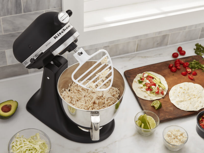 KitchenAid® stand mixer on a modern kitchen counter shredding cooked chicken. KitchenAid® stand mixer on a modern kitchen counter shredding cooked chicken.