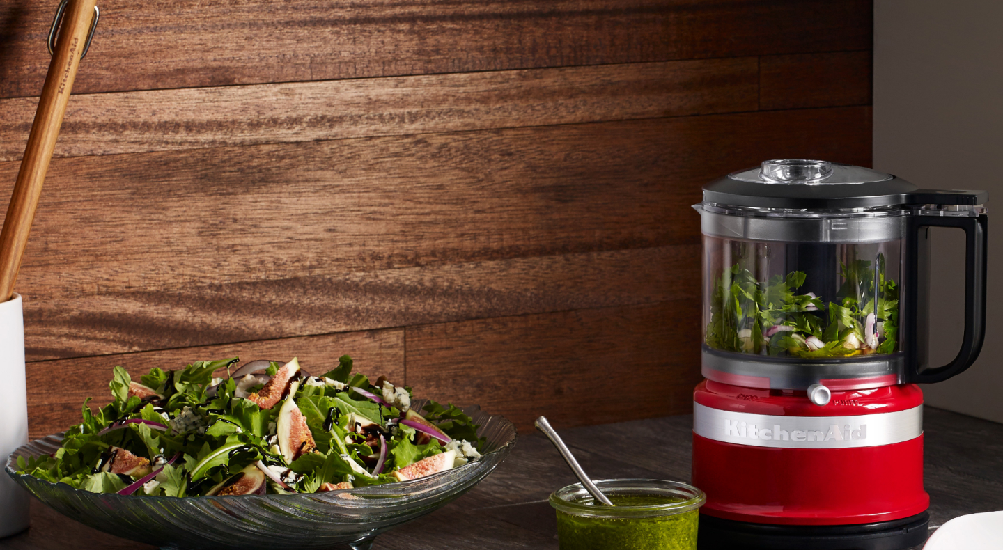 Small red food processor filled with mixed greens next to tossed salad on counter Small red food processor filled with mixed greens next to tossed salad on counter