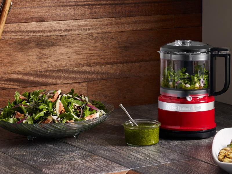 Small red food processor filled with mixed greens next to tossed salad on counter Small red food processor filled with mixed greens next to tossed salad on counter