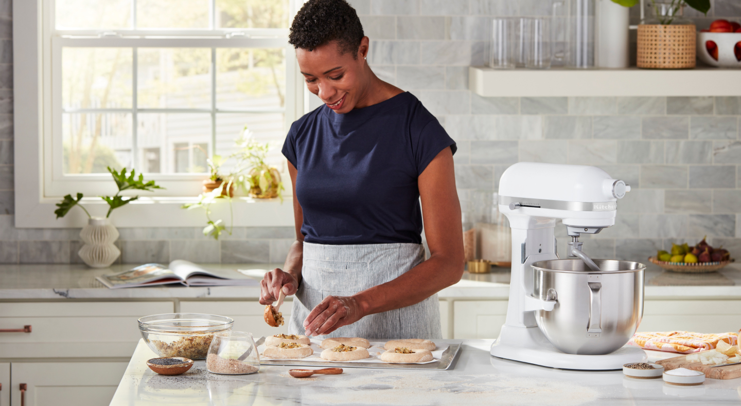 Person sprinkling herbs and seeds on top of shaped bagel dough Person sprinkling herbs and seeds on top of shaped bagel dough