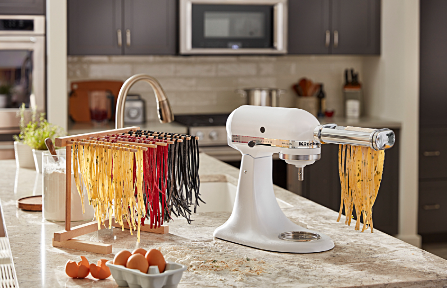 Three different colors of homemade spaghetti noodles drying beside a stand mixer