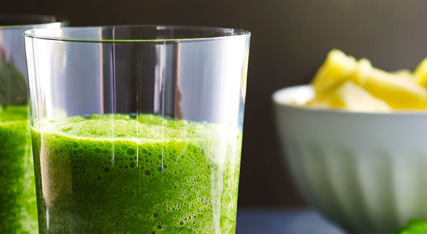 A bowl of fruit next to a glass of kale juice A bowl of fruit next to a glass of kale juice