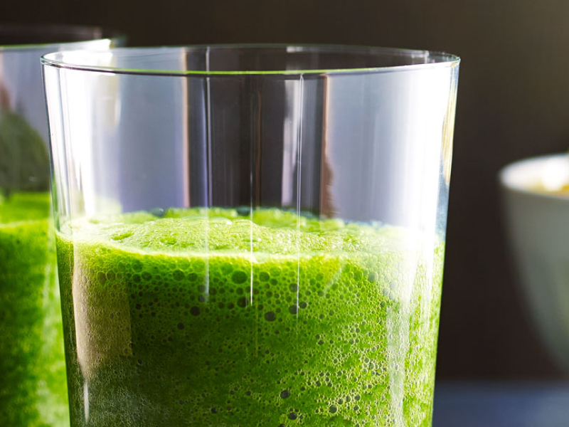 A bowl of fruit next to a glass of kale juice A bowl of fruit next to a glass of kale juice