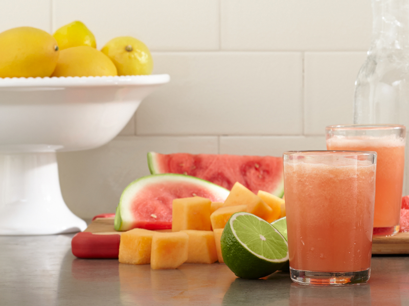 Glasses of fresh juice next to assorted fruit pieces Glasses of fresh juice next to assorted fruit pieces