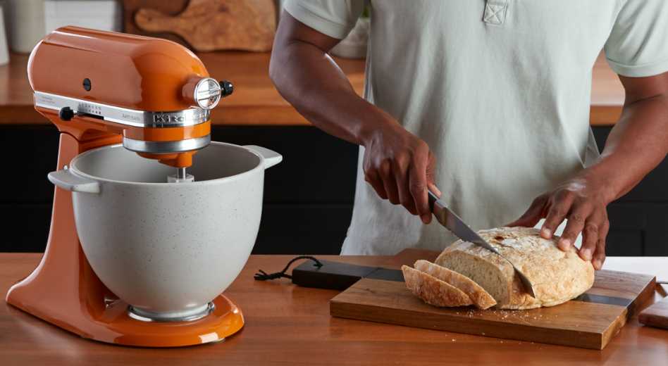 An orange stand mixer and a person slicing homemade bread. An orange stand mixer and a person slicing homemade bread.