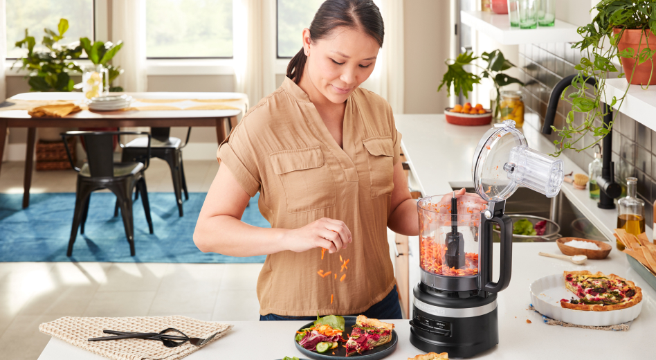 A person using a food processor filled with shredded carrots A person using a food processor filled with shredded carrots