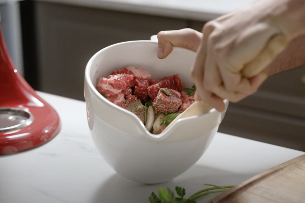 Cubed meat in a KitchenAid brand stand mixer bowl with seasoning