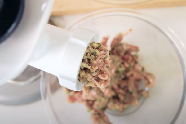 Close-up of seasoned ground beef moving through meat grinder