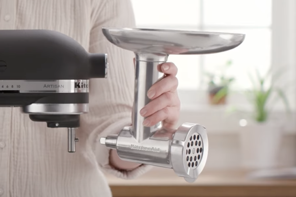 Person holding metal food grinder near stand mixer