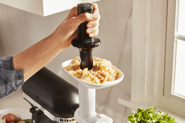 Person using food pusher to feed meat through white food grinder