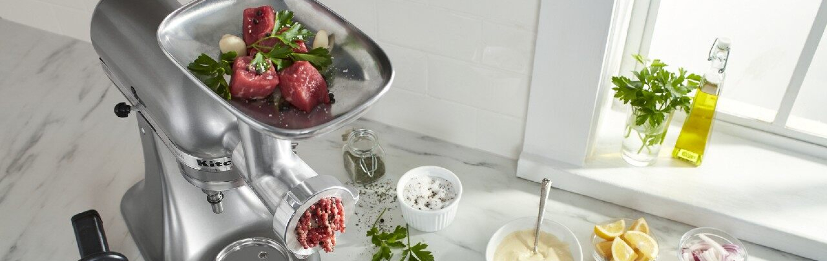 KitchenAid® Stand Mixer with food grinder attachment grinding meat on counter with ingredients