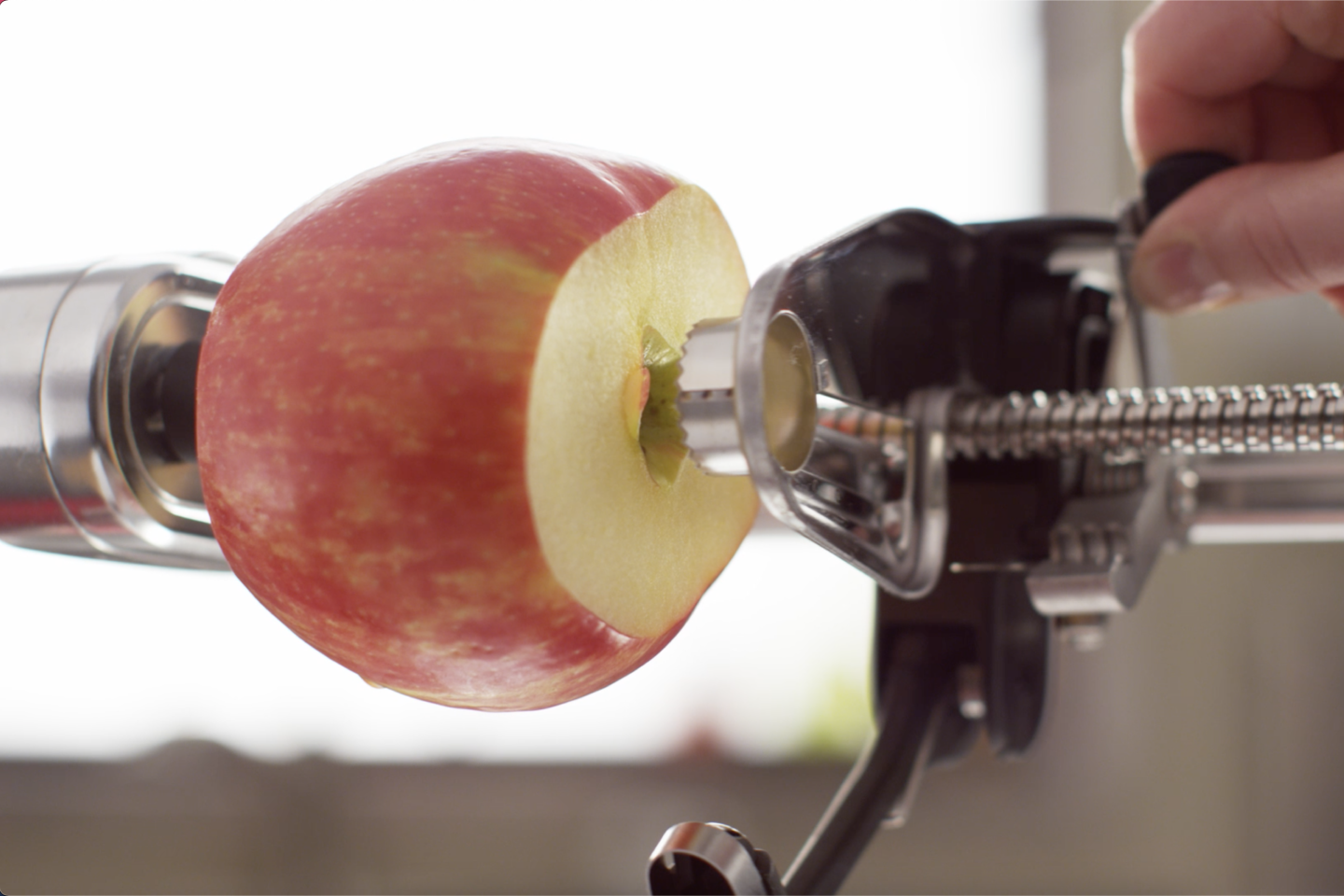 A person coring an apple with a stand mixer attachment. A person coring an apple.