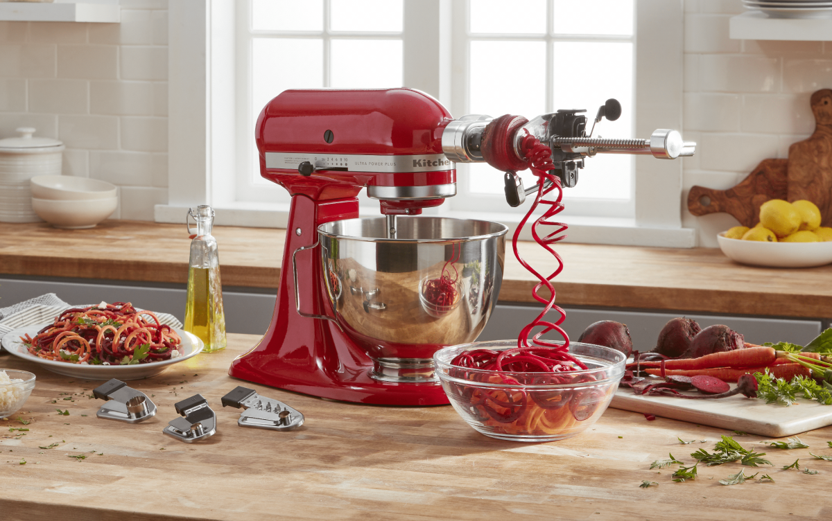 Spiralizer attachment spiralizing vegetables attached to red KitchenAid® stand mixer