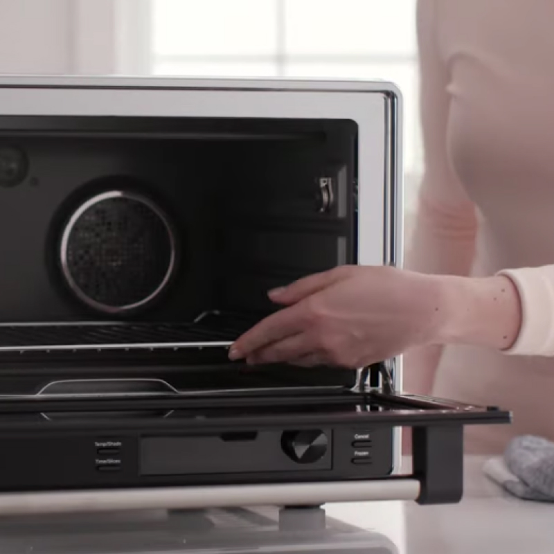 Person placing air fryer tray inside of black air fryer.