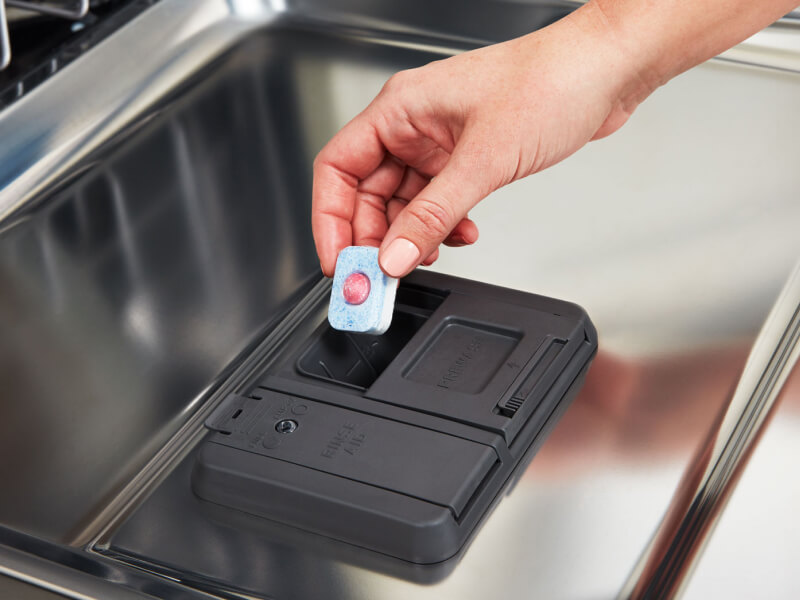 Person loading pod detergent into detergent compartment in dishwasher