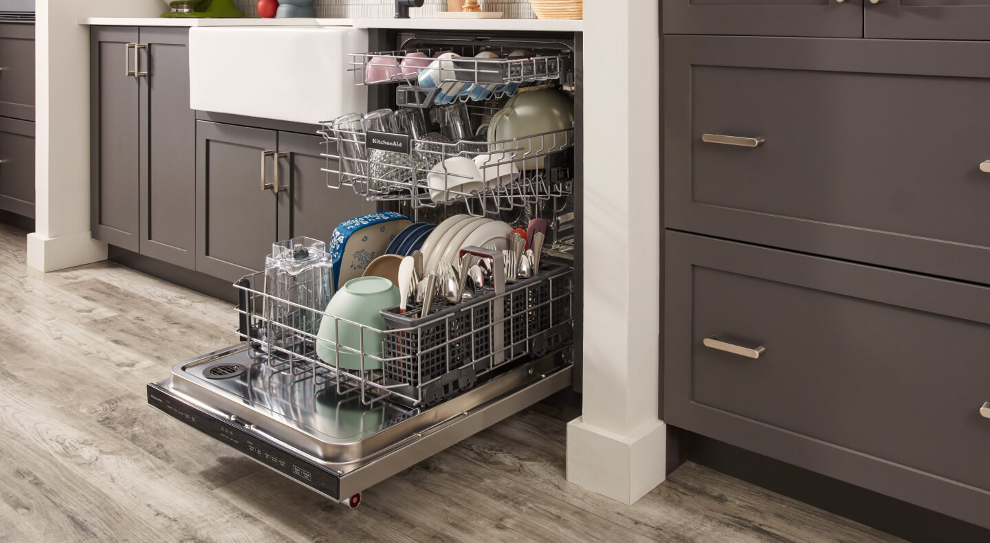 An opened KitchenAid® dishwasher with three fully loaded racks
