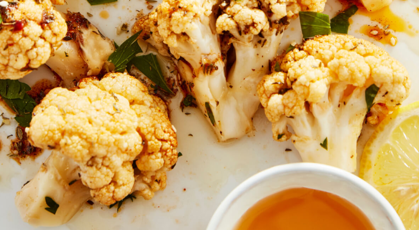 Honey roasted cauliflower with small pot of honey and lemon slice in foreground.