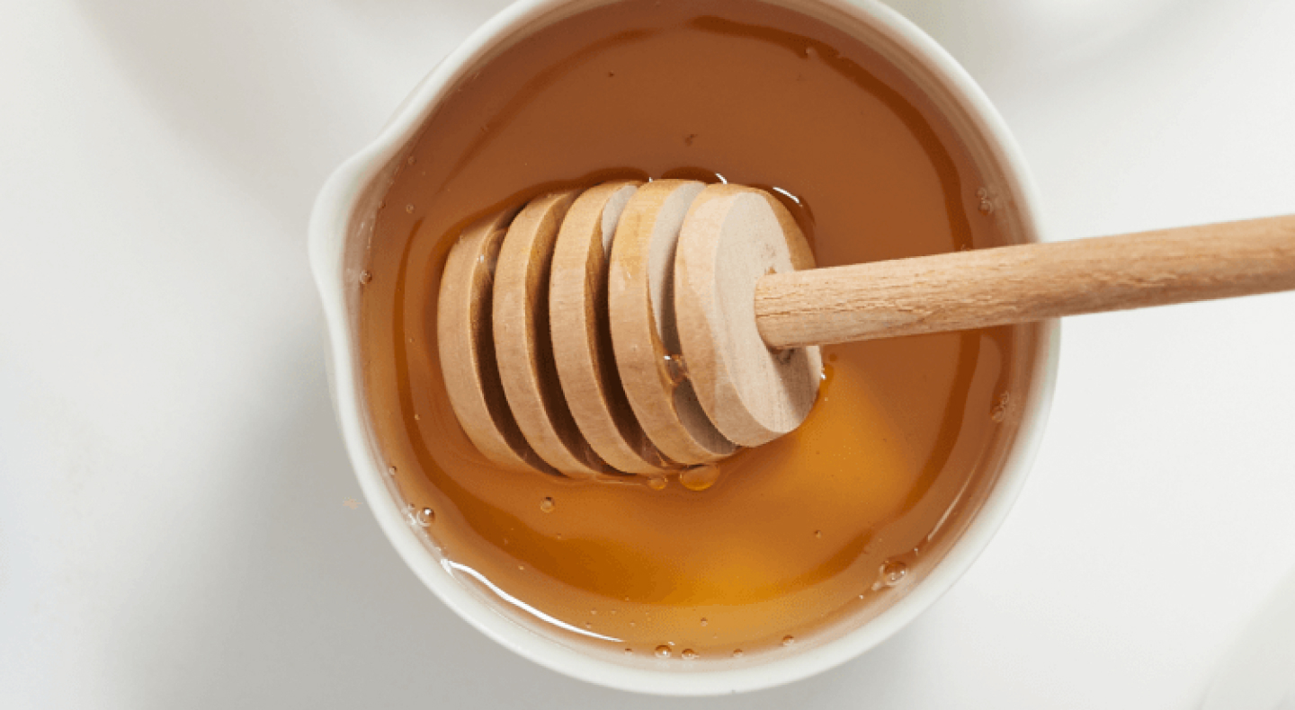 White pot of honey with honey dipper.