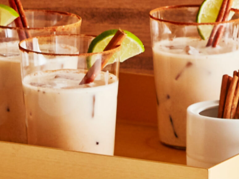 Tray holding three cocktails garnished with limes and cinnamon sticks.