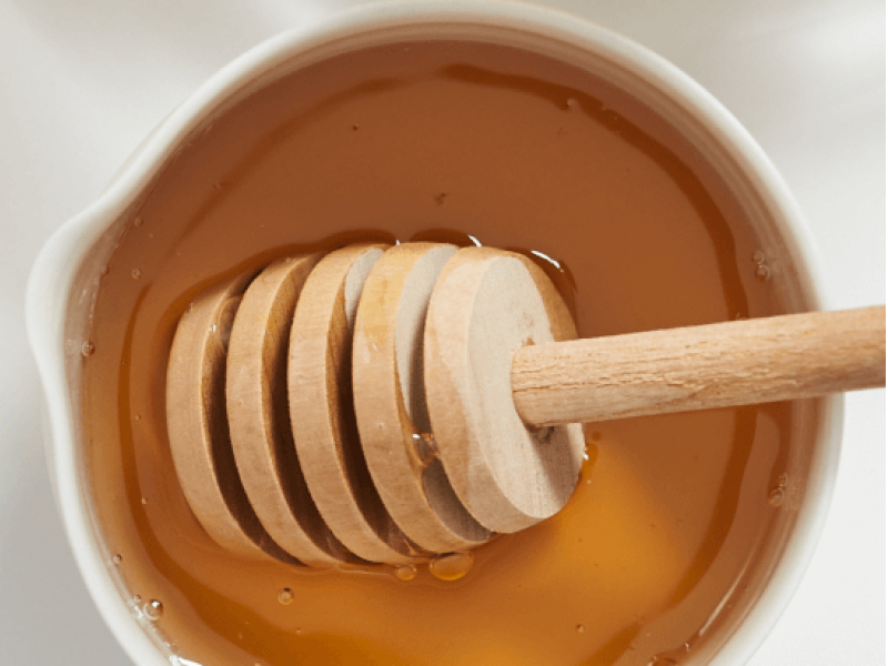 White pot of honey with honey dipper.