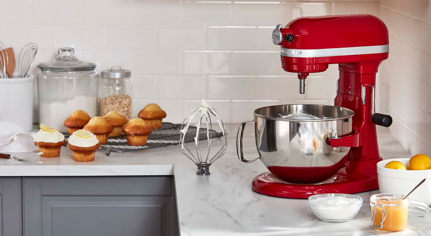 KitchenAid® stand mixer next to a wire whip accessory with stiff egg white peaks and frosted muffins in modern kitchen. KitchenAid® stand mixer next to a wire whip accessory with stiff egg white peaks and frosted muffins in modern kitchen.