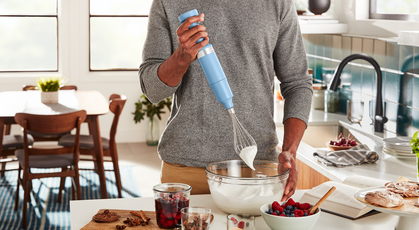 A man using a KitchenAid® hand blender to whip egg white peaks in a modern kitchen.  A man using a KitchenAid® hand blender to whip egg white peaks in a modern kitchen.
