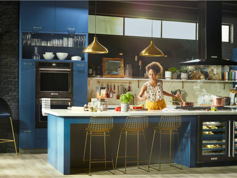 Woman cooking in a kitchen with black stainless steel KitchenAid® appliances Woman cooking in a kitchen with black stainless steel KitchenAid® appliances