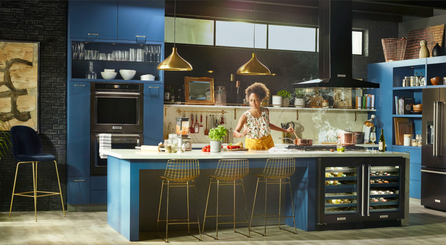Woman cooking in a kitchen with black stainless steel KitchenAid® appliances Woman cooking in a kitchen with black stainless steel KitchenAid® appliances
