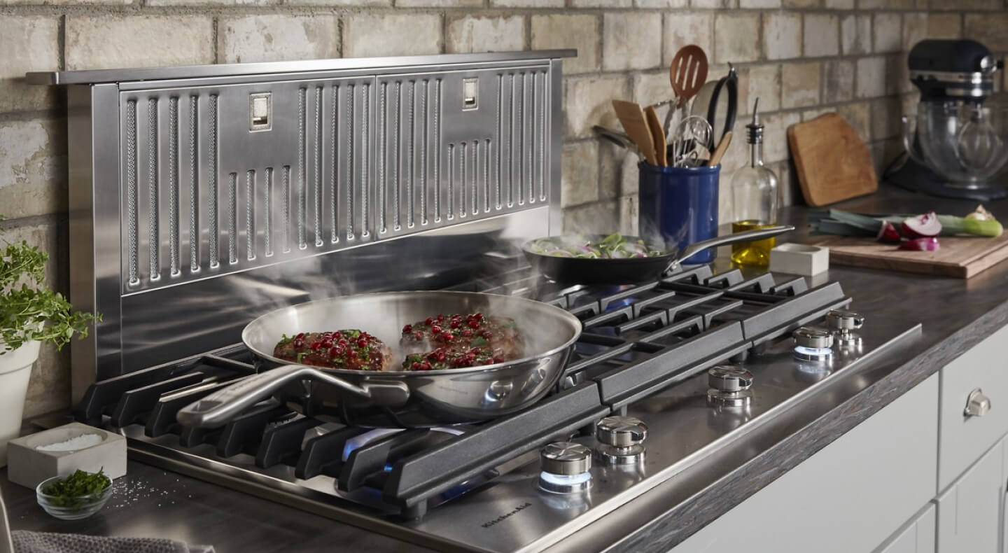 Food cooking in front of a retractable downdraft vent