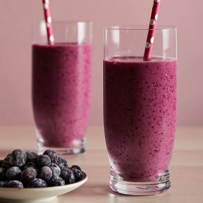 Two purple smoothies near a plate of frozen blueberries