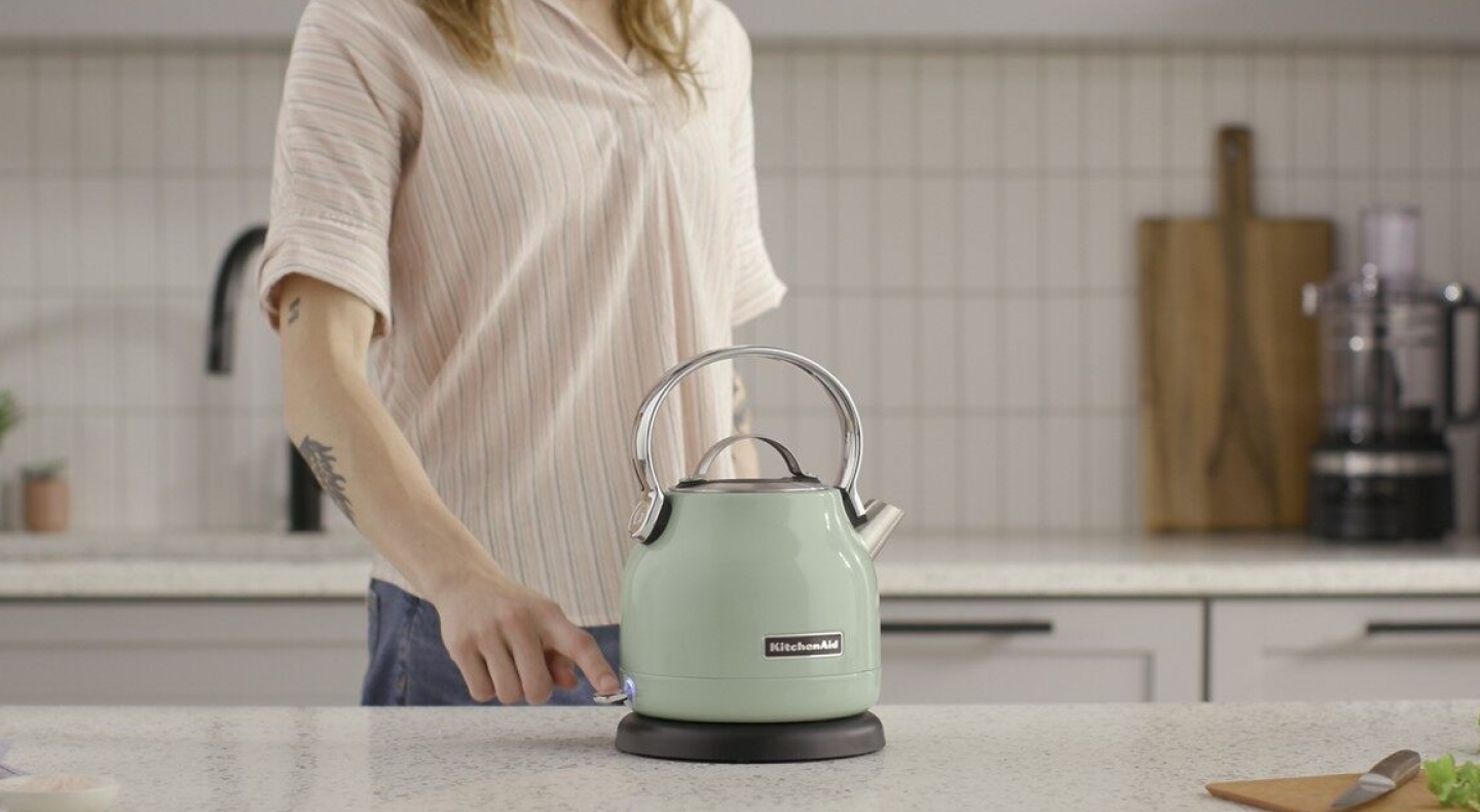 Woman standing by a green KitchenAid® electric kettle Woman standing by a green KitchenAid® electric kettle