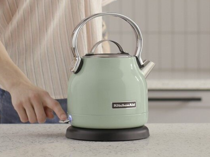 Woman standing by a green KitchenAid® electric kettle Woman standing by a green KitchenAid® electric kettle