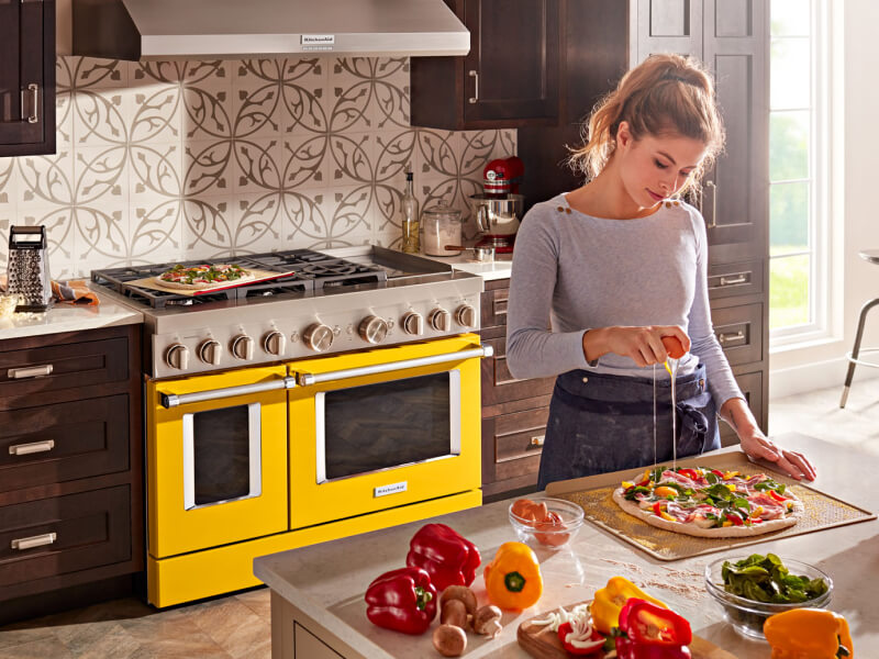 Yellow KitchenAid® range behind person preparing food at a kitchen island Yellow KitchenAid® range behind person preparing food at a kitchen island