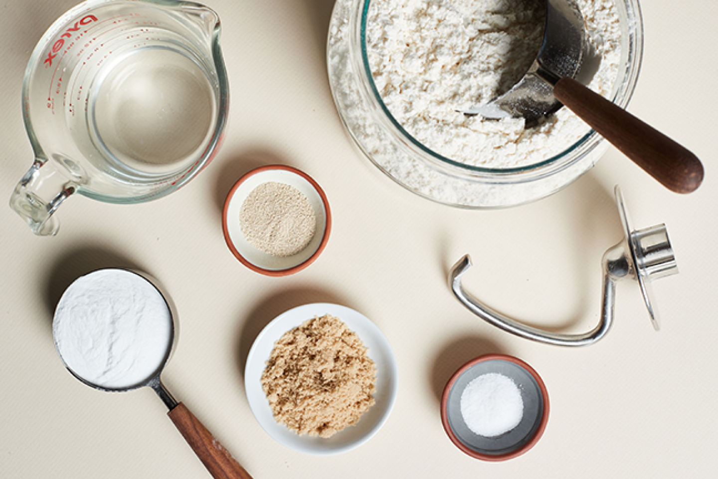 Dough ingredients and measuring cups next to a dough hook Dough ingredients and measuring cups next to a dough hook