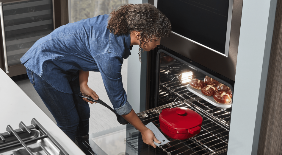 Woman placing red dutch oven in oven with homemade pretzel rolls baking on upper rack Woman placing red dutch oven in oven with homemade pretzel rolls baking on upper rack