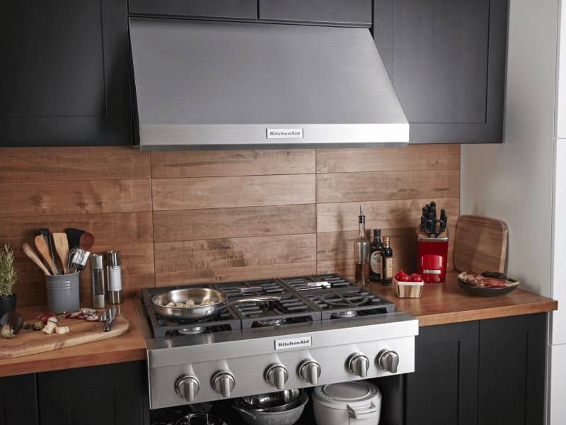 Stainless steel gas range and range hood set into a wooden countertop and backsplash