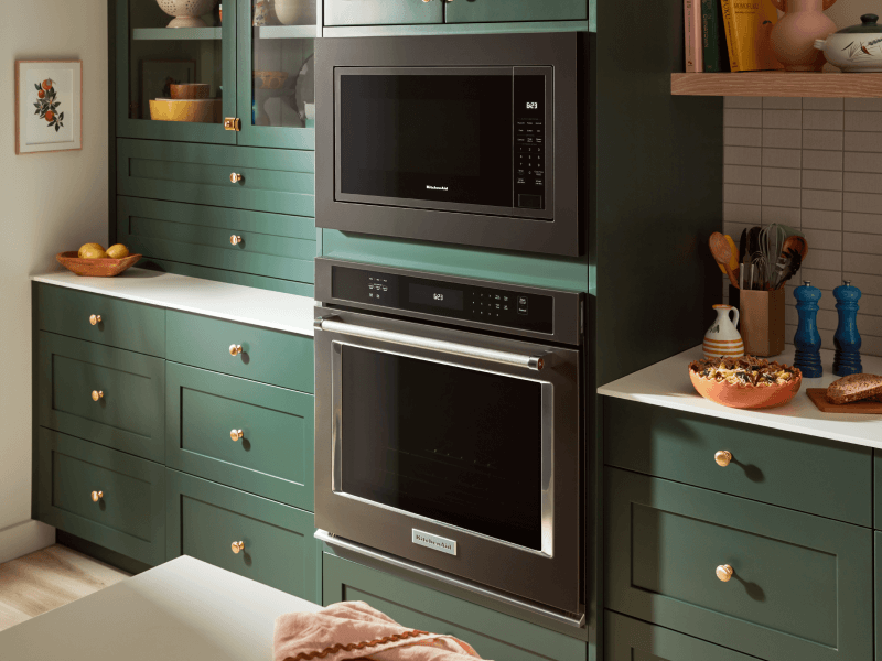 Stainless steel wall oven and black microwave set into deep green cabinetry