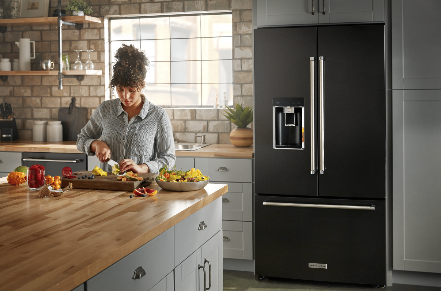 A person slicing fruit and a black KitchenAid® refrigerator. A person slicing fruit and a black KitchenAid® refrigerator.