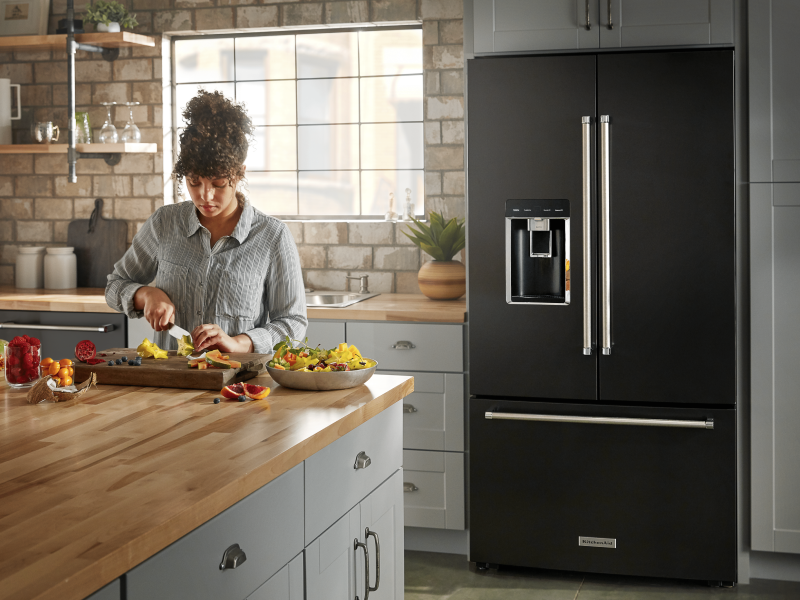 A person slicing fruit and a black KitchenAid® refrigerator. A person slicing fruit and a black KitchenAid® refrigerator.