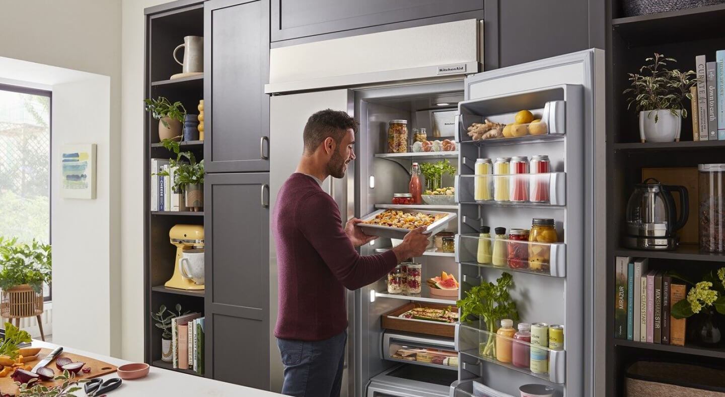 Person sliding a tray of food into a side-by-side refrigerator