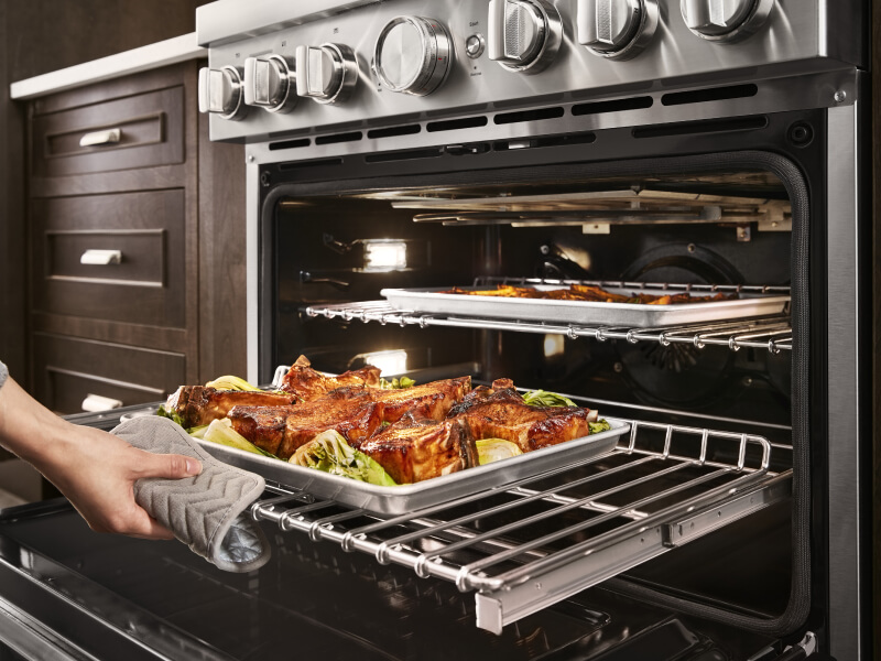 Person pulling a baking tray of roasted meat out of a KitchenAid® oven