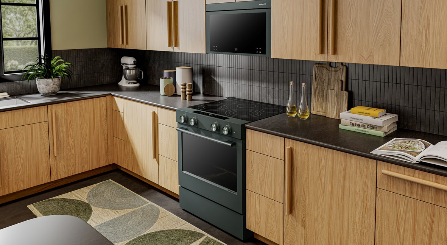 The corner of a modern kitchen with wood cabinets and a range in juniper green